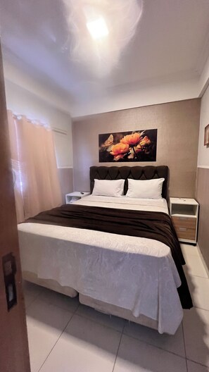 Une chambre à coucher avec un lit, une table de chevet, un tableau accroché au mur et un luminaire au plafond.