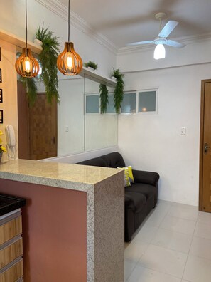 A reception area with a counter, a black sofa, hanging plants, and a ceiling fan. - 206 Versátil e Aconchegante (Belém)