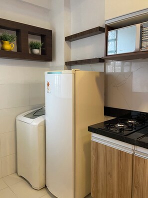 A compact kitchen with a built-in gas stove, a white refrigerator, and a washing machine. - 206 Versátil e Aconchegante (Belém)