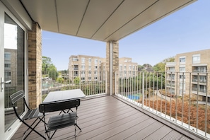 Ein Balkon mit Tisch und Stühlen, der auf einen Wohnbereich mit Ziegelgebäuden und einem Schwimmbad blickt.