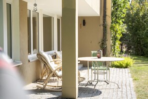 A patio with wicker chairs and a metal table, a window with a view of greenery, and a wall with a small window. - Chasa Val 739 - Spacious vacation home with a garden sauna and hot tub in Scuol (Scuol)