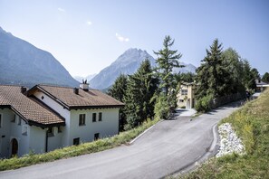 Eine Straße führt zu einem Bergdorf mit traditionellen Häusern, wolkenlosem Himmel und Blick auf die Berge.
