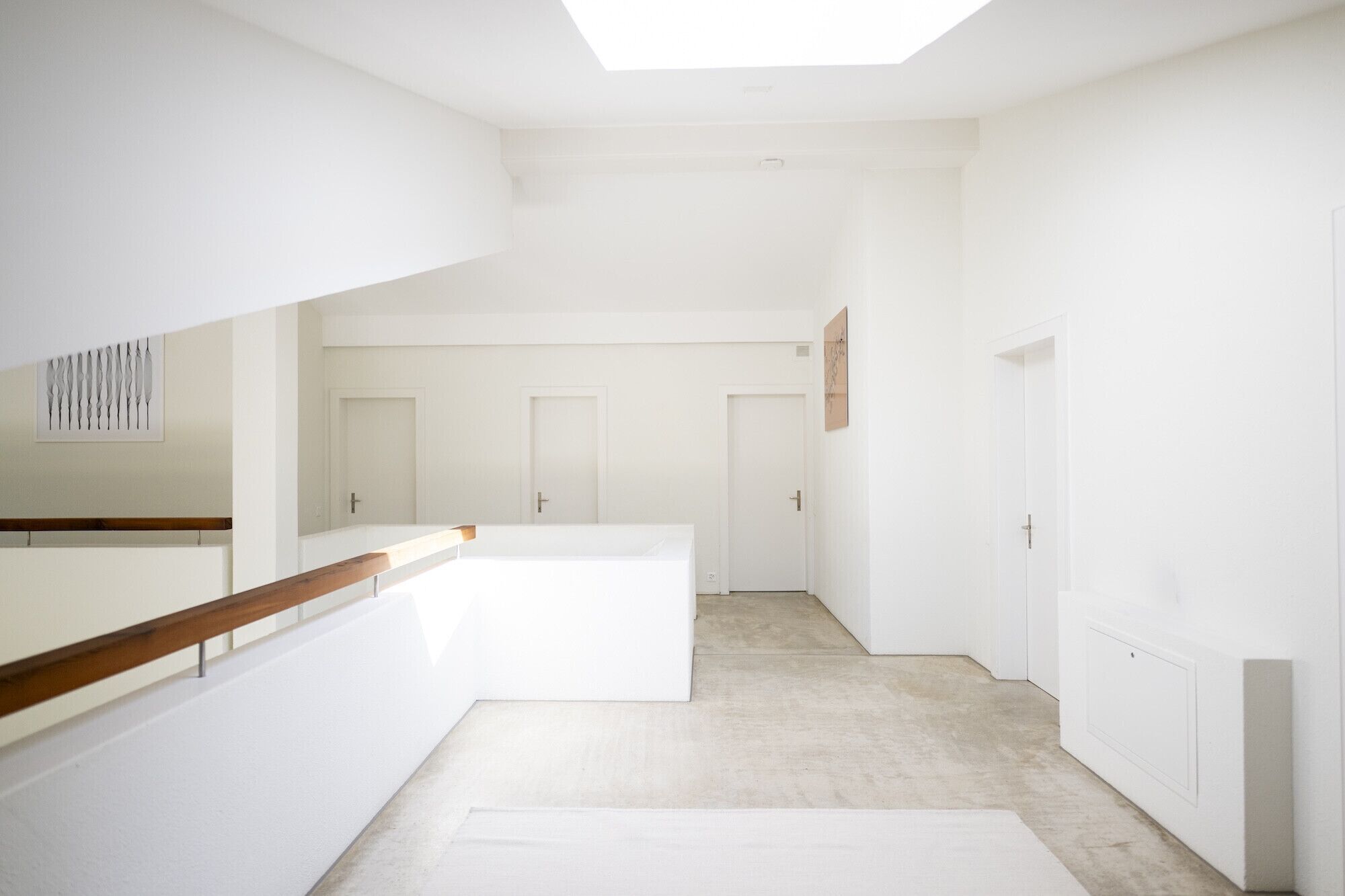 Ruime, goed verlichte ruimte met een hoge plafond, een houten leuning, en zicht op een deur aan het einde van een gang.