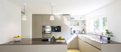 Une cuisine moderne dotée d’un îlot central, d’appareils électroménagers intégrés et d’une fenêtre laissant entrer la lumière naturelle.