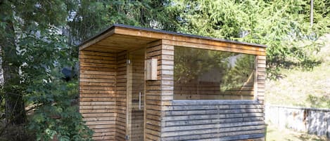 Una cabaña de madera pequeña con puerta de vidrio, rodeada de abundante vegetación.