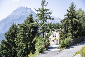 Eine Bergstraße mit einem Gebäude, umgeben von Bäumen, mit Blick auf ein Gebirge.