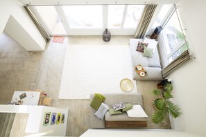 Quarto com pé direito alto, uma grande janela, um sofá, uma mesa de centro e uma pequena mesa lateral.