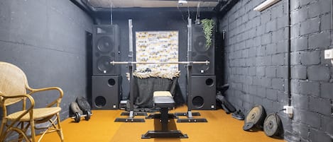 A room with a black brick wall, a yellow carpet, a black exercise bench, and a wicker chair.