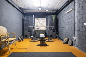 A room with a black brick wall, a yellow carpet, a black exercise bench, and a wicker chair. - Chasa Val 739 - Spacious vacation home with a garden sauna and hot tub in Scuol (Scuol)