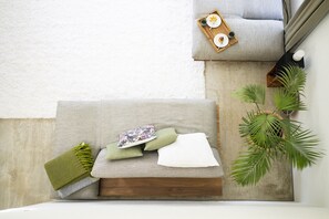 Ein ordentlich eingerichteter Sitzbereich mit einer Couch, Kissen, einem Tablett mit Tellern und Tassen sowie einer Zimmerpflanze.