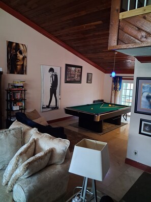 A room with a pool table, a sofa, a lamp, and artwork on the walls.