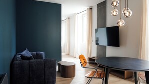 Ein modernes Wohnzimmer mit einem dunkelgrauen Sofa, einem runden Tisch und einem Flachbildfernseher an der Wand.