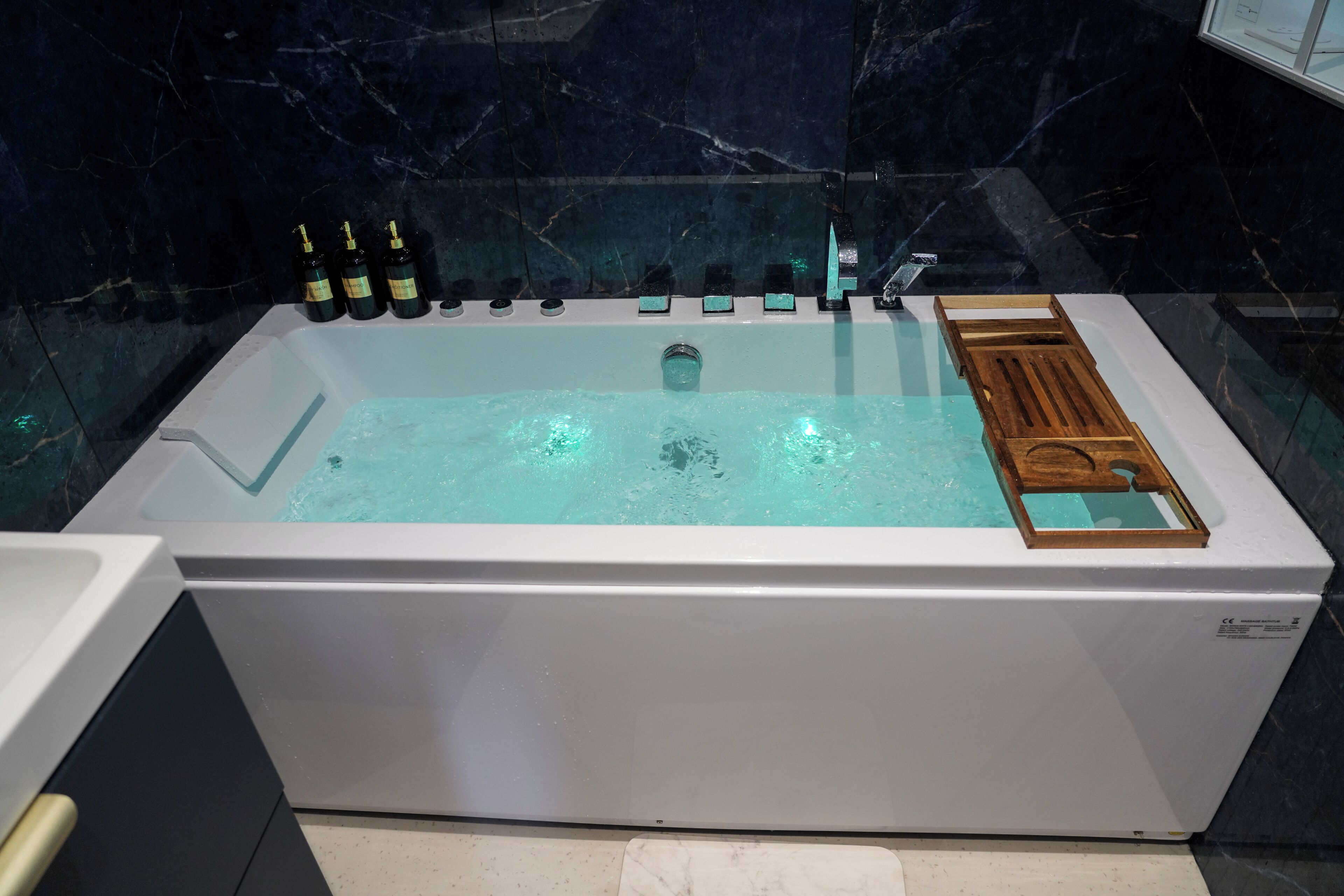 A modern bathroom with a large bathtub, a wooden tray, and several bottles of shampoo and conditioner.