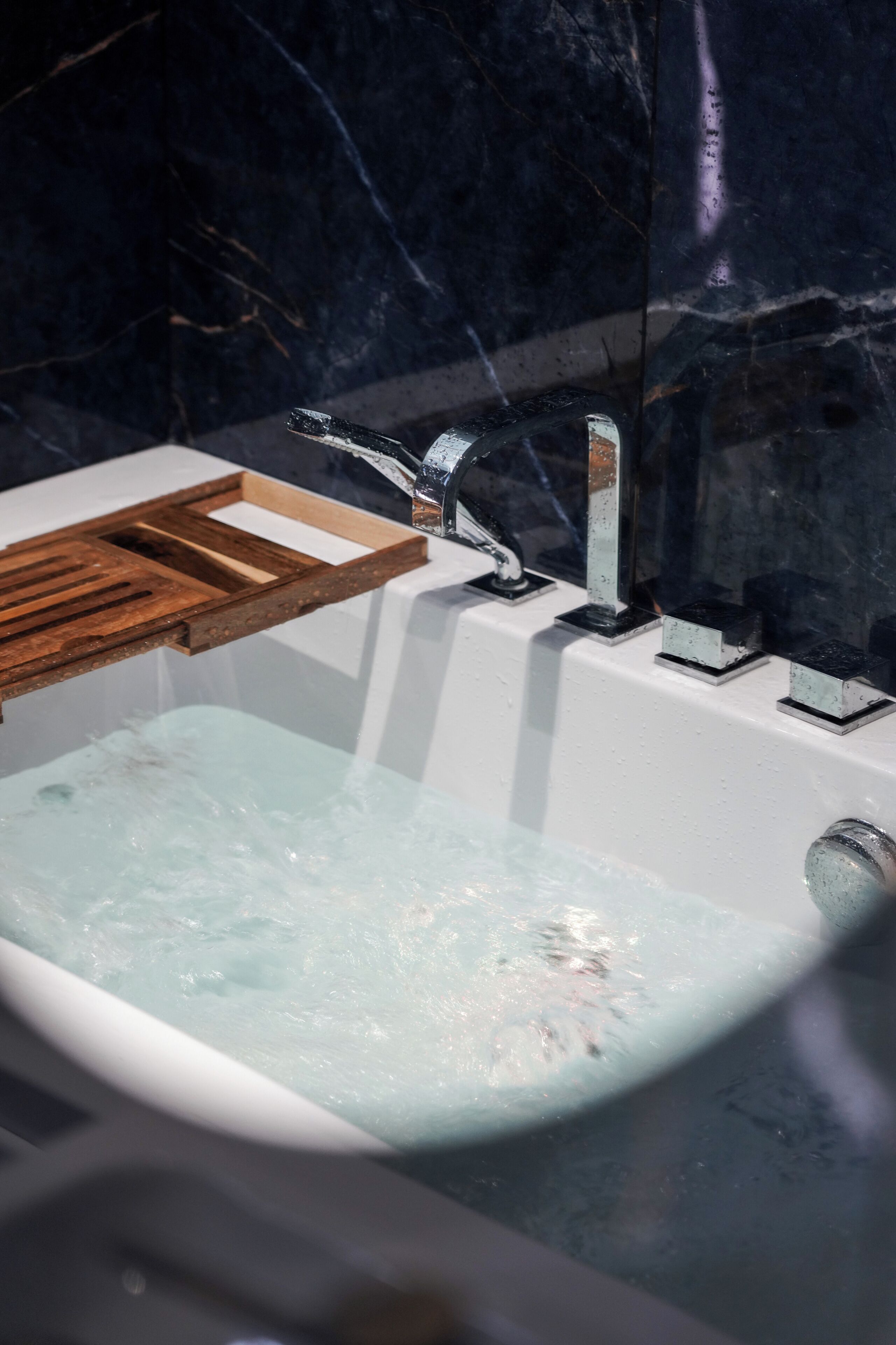 A bathtub with a wooden tray and a modern faucet.