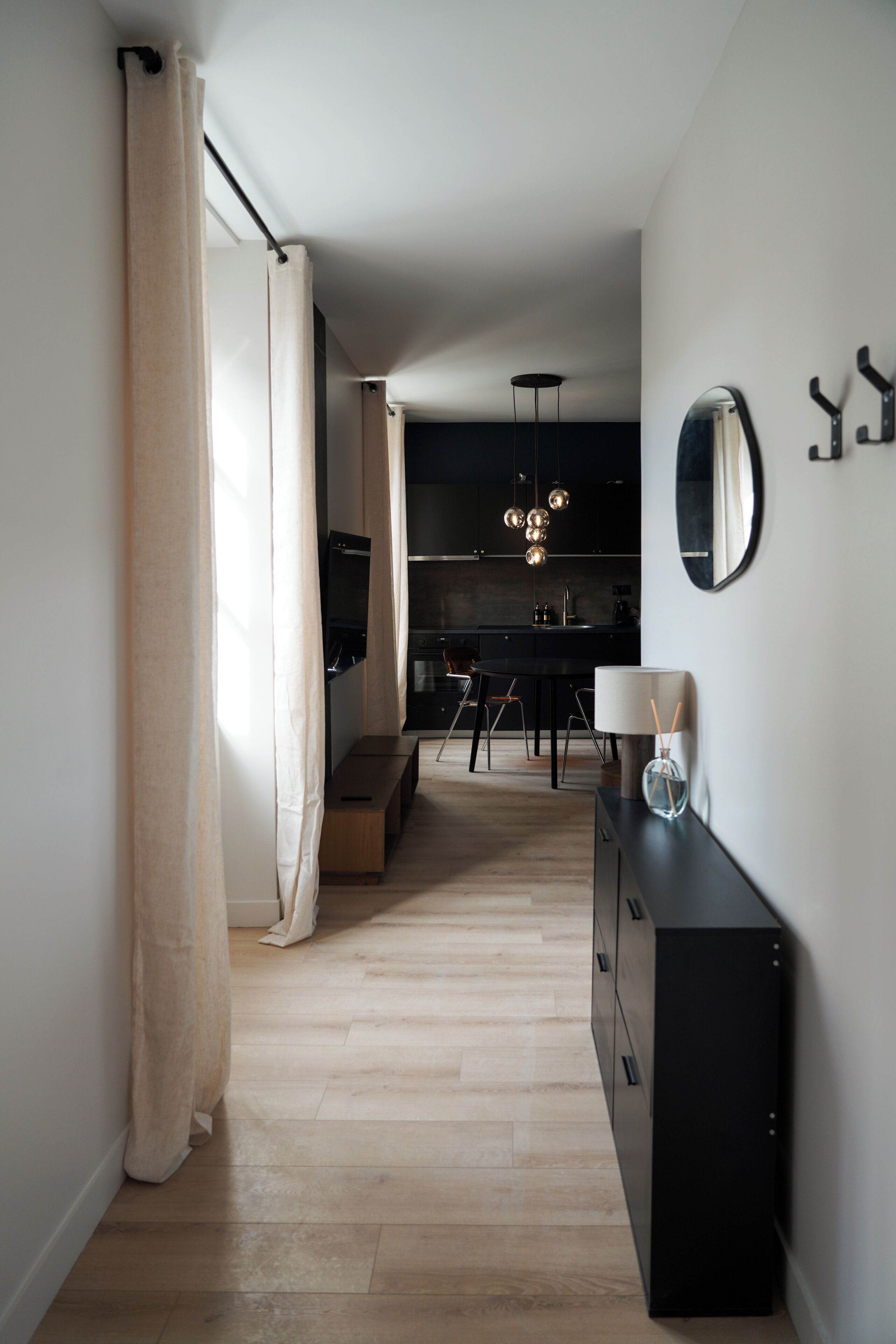 A modern kitchen with a central island, a dining area with chairs, and a hallway leading to a bedroom.