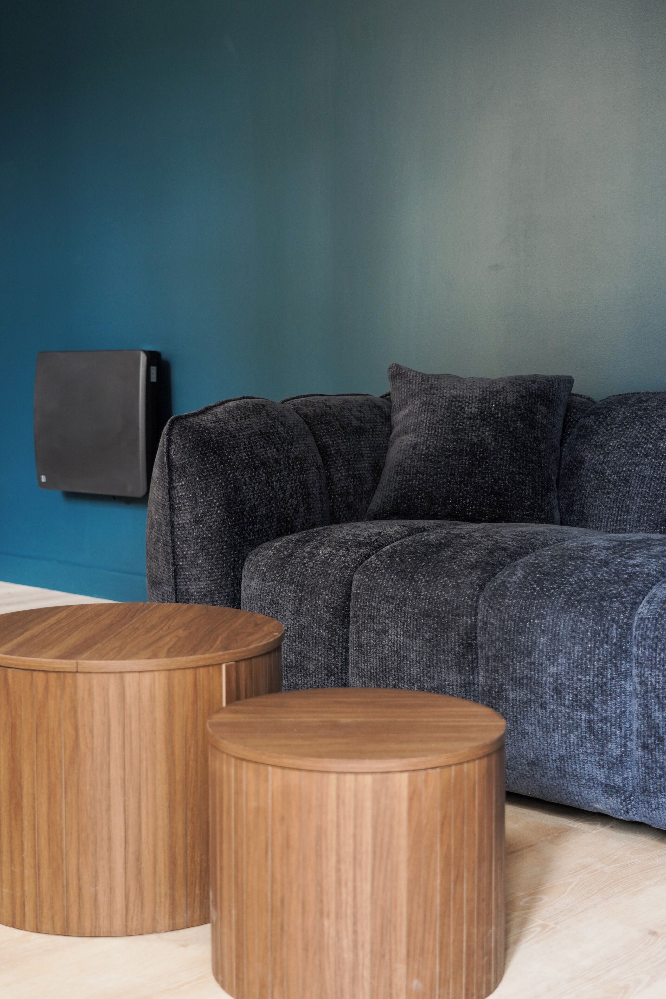 Ein Zimmer mit blauer Wand, grauem Sofa und zwei Holznachttischen.