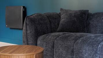 Een kamer met een blauwe wand, een grijze bank en twee houten bijzettafeltjes.