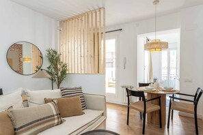 A modern living room with a sofa, dining table, chairs, and a mirror. - Beautiful one-bedroom apartment on Calle Castillo, Madrid, perfect for extended stays. Mediterranean style blends seamlessly with rustic touches of exposed brick and natural wood, creating a warm, bright, and inviting atmosphere. (MADRID)