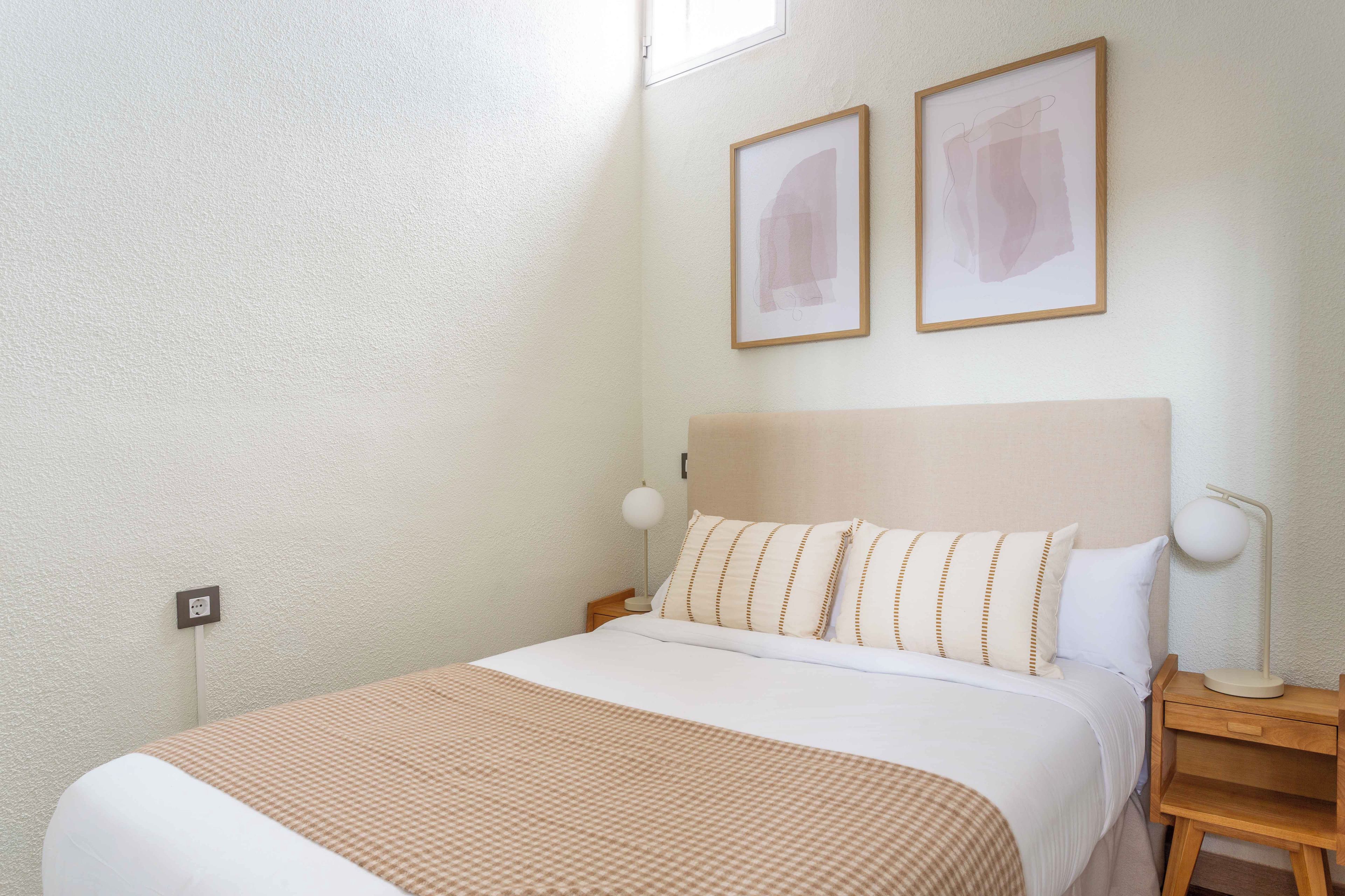 A neatly made bed with a checkered blanket, a bedside table with a lamp, and two framed pictures on the wall.