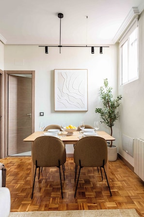 A dining area with a wooden table, two chairs, a plant, and a framed artwork on the wall. - Private and quiet on Cuesta de Santo Domingo, this three bedroom apartment sits in one of the best locations in Madrid, with the Royal Palace and Teatro Real just steps away and Puerta del Sol and Plaza Mayor an easy walk beyond. (MADRID)