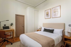 A bedroom with a bed, a desk with a laptop, a chair, and two bedside tables with lamps. - Private and quiet on Cuesta de Santo Domingo, this three bedroom apartment sits in one of the best locations in Madrid, with the Royal Palace and Teatro Real just steps away and Puerta del Sol and Plaza Mayor an easy walk beyond. (MADRID)