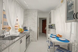 Een kleine keuken met een spoelbak, aanrecht en een eethoek met een tafel en stoelen.