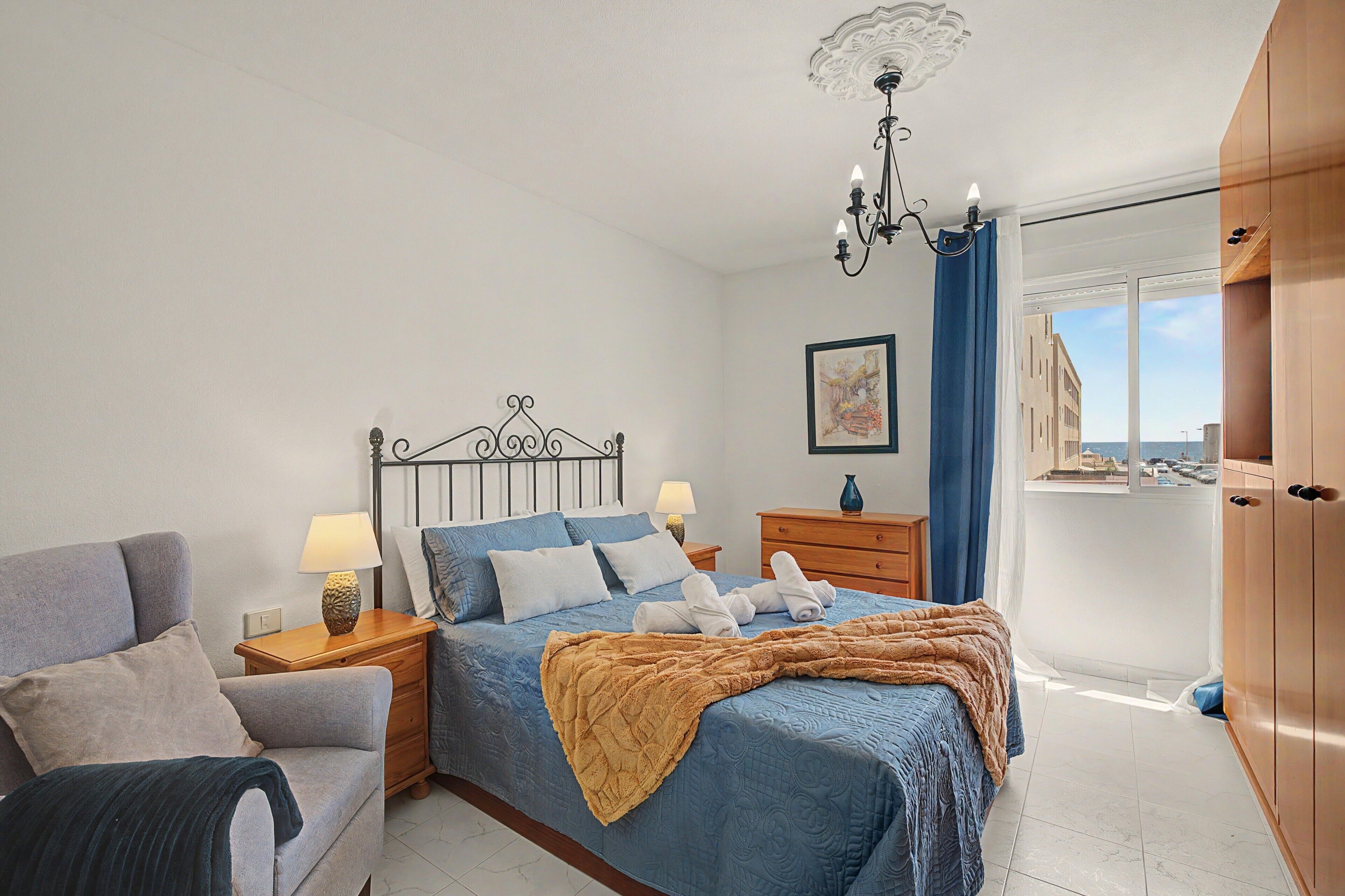 Une chambre à coucher comprenant un lit, des tables de chevet, une lampe, une chaise, une armoire et une fenêtre donnant sur un beau paysage.
