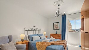 Une chambre à coucher comprenant un lit, des tables de chevet, une lampe, une chaise, une armoire et une fenêtre donnant sur un beau paysage.