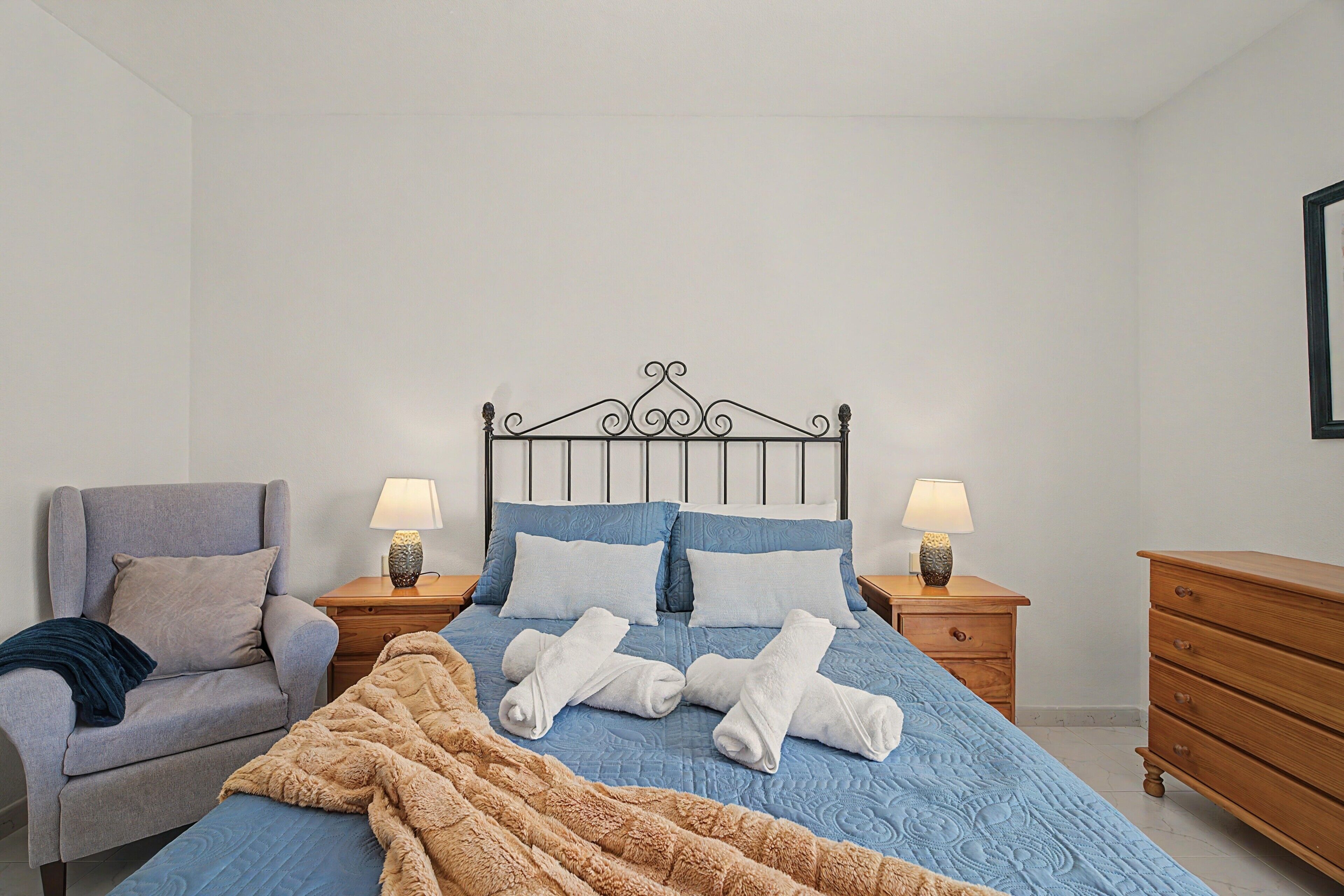 Un dormitorio con una cama, dos mesitas de noche, una silla y un aparador de madera.