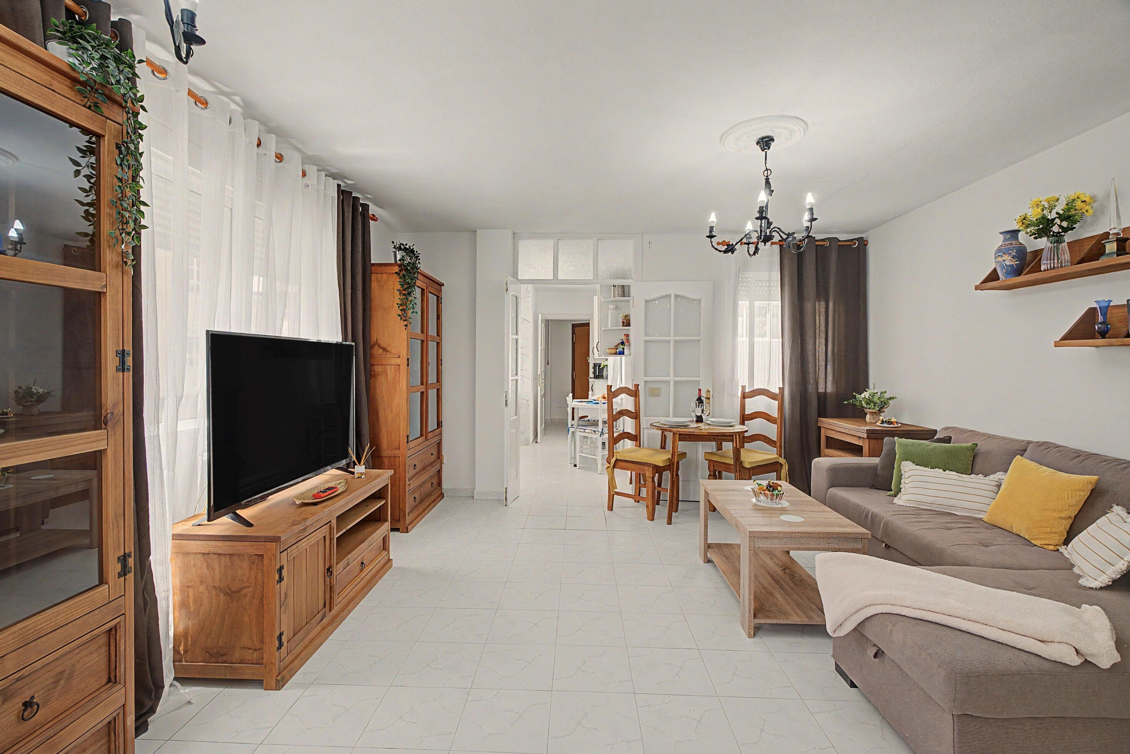 Un salon moderne doté d’un téléviseur à écran plat, de meubles en bois, d’un coin repas avec des chaises et d’un canapé agrémenté de coussins.