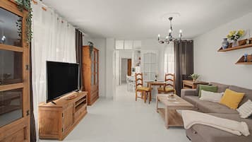 A modern living room with a flat-screen TV, wooden furniture, a dining area with chairs, and a sofa with cushions.