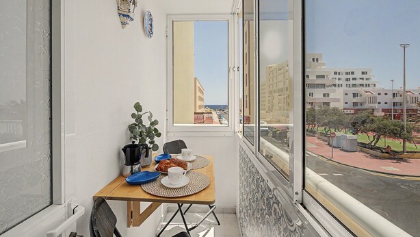 Un petit balcon avec une table dressée pour deux personnes, un pot de fleurs et une vue sur une rue et des immeubles.