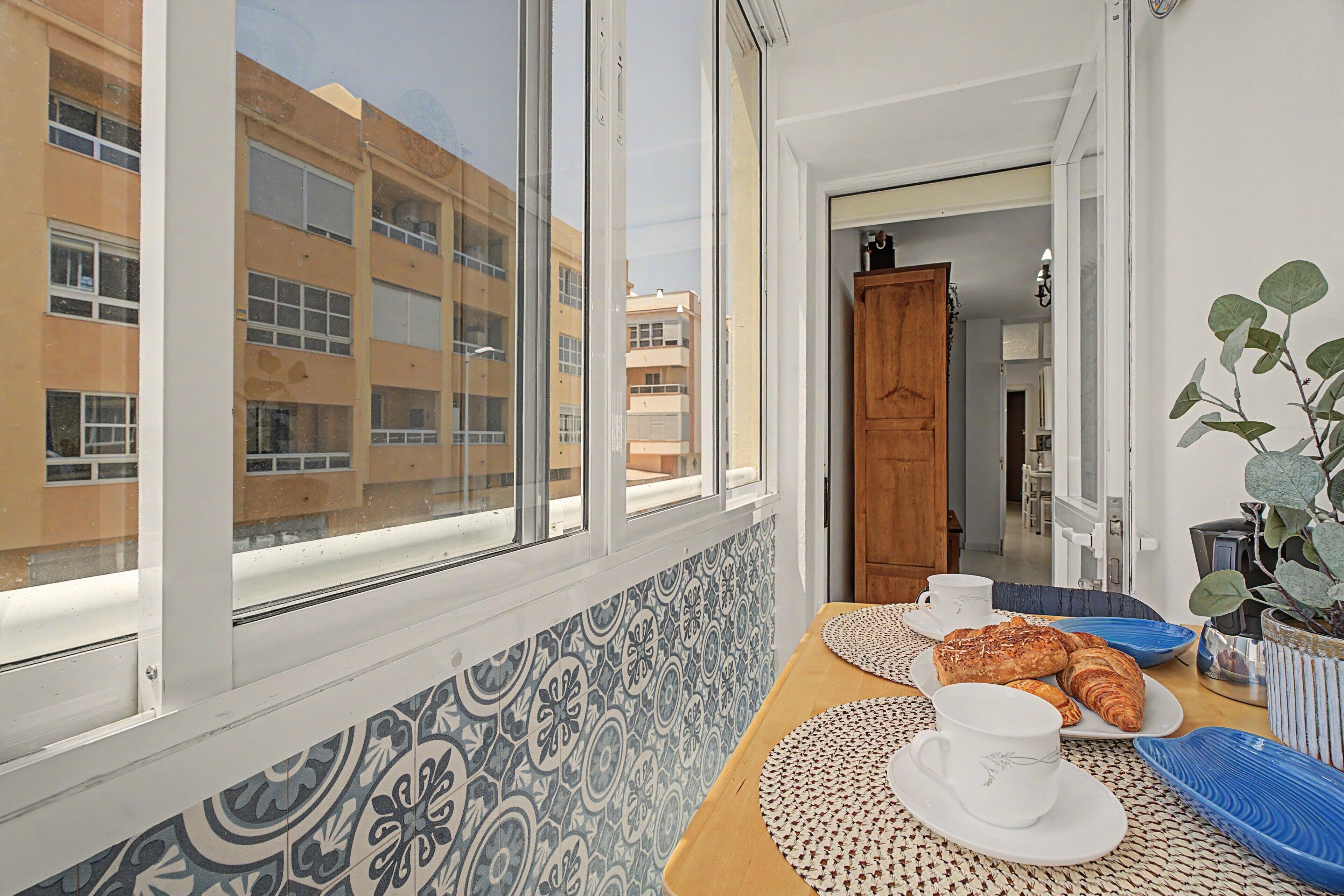 Une pièce dotée d’une grande fenêtre, d’un mur orné de motifs, d’une porte en bois et d’une table sur laquelle sont disposés des aliments pour le petit-déjeuner.