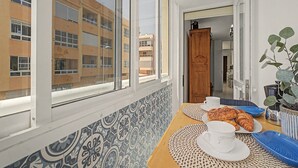 Une pièce dotée d’une grande fenêtre, d’un mur orné de motifs, d’une porte en bois et d’une table sur laquelle sont disposés des aliments pour le petit-déjeuner.