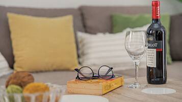 Een fles Merlot wijn, een wijnglas, een paar brillen en een boek op een houten tafel.