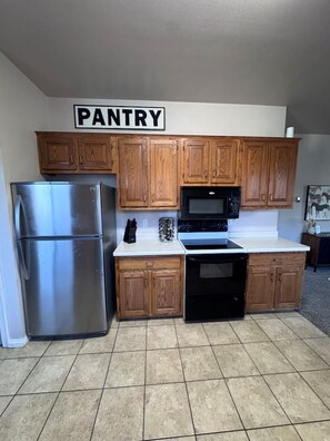 A kitchen with wooden cabinets, a stainless steel refrigerator, a microwave, and a stove.