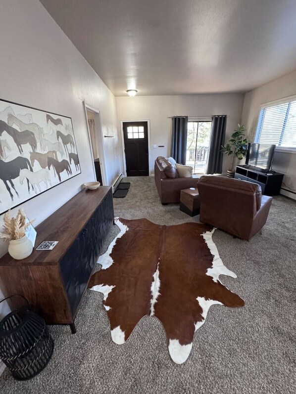 A living room with a brown and white rug, a sofa, a coffee table, a TV, and a painting on the wall.