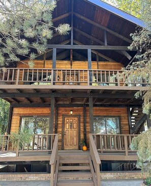 A two-story wooden cabin with a balcony, a front door, and a staircase leading to the entrance.