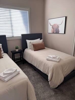 A hotel room with two beds, a small table with a plant, and a framed picture on the wall.