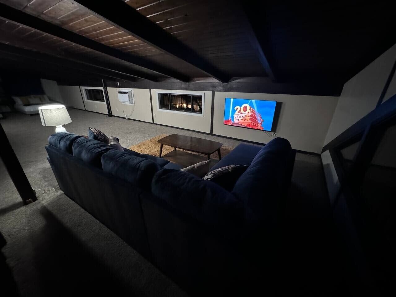 Uma sala de estar com um sofá azul escuro, uma mesa de centro e uma televisão de tela plana fixada na parede.