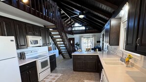 A kitchen with dark cabinetry, a white refrigerator, a stove, and a sink. There is a staircase leading to an upper level.
