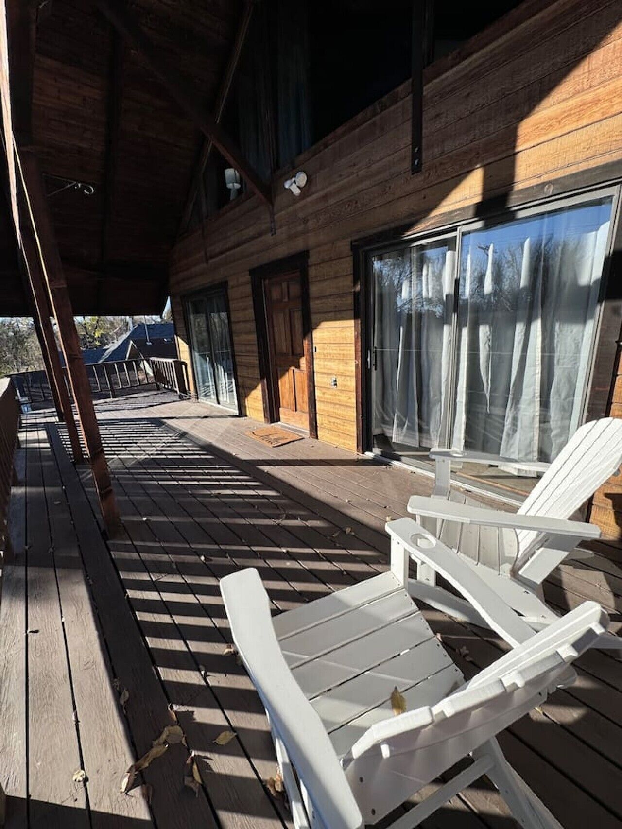 Una terraza de madera con sillas Adirondack, un área cubierta y un edificio con grandes ventanales.