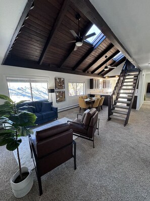A spacious living area with a high ceiling, a staircase, and a dining area.