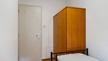 Quarto pequeno com guarda-roupa de madeira, porta branca e estrutura de cama de metal.