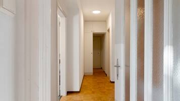 Un couloir aux murs blancs, doté d’un plancher en bois et d’une porte en verre dépoli.