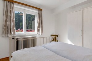 Un dormitori amb llit, un radiador, una finestra amb cortines i vista a un bosc.