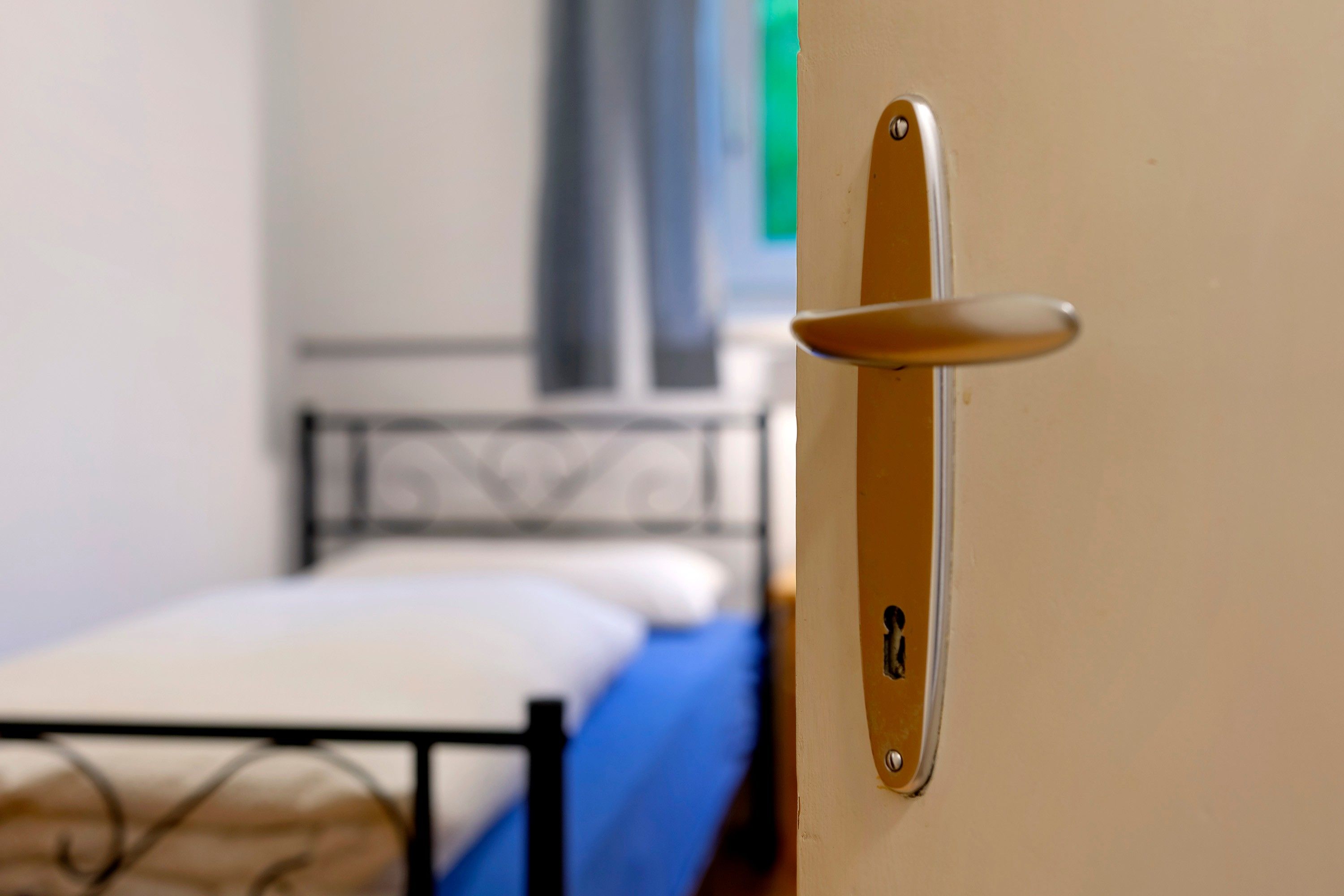Une porte avec une poignée, un lit avec un matelas bleu et une tête de lit en métal.