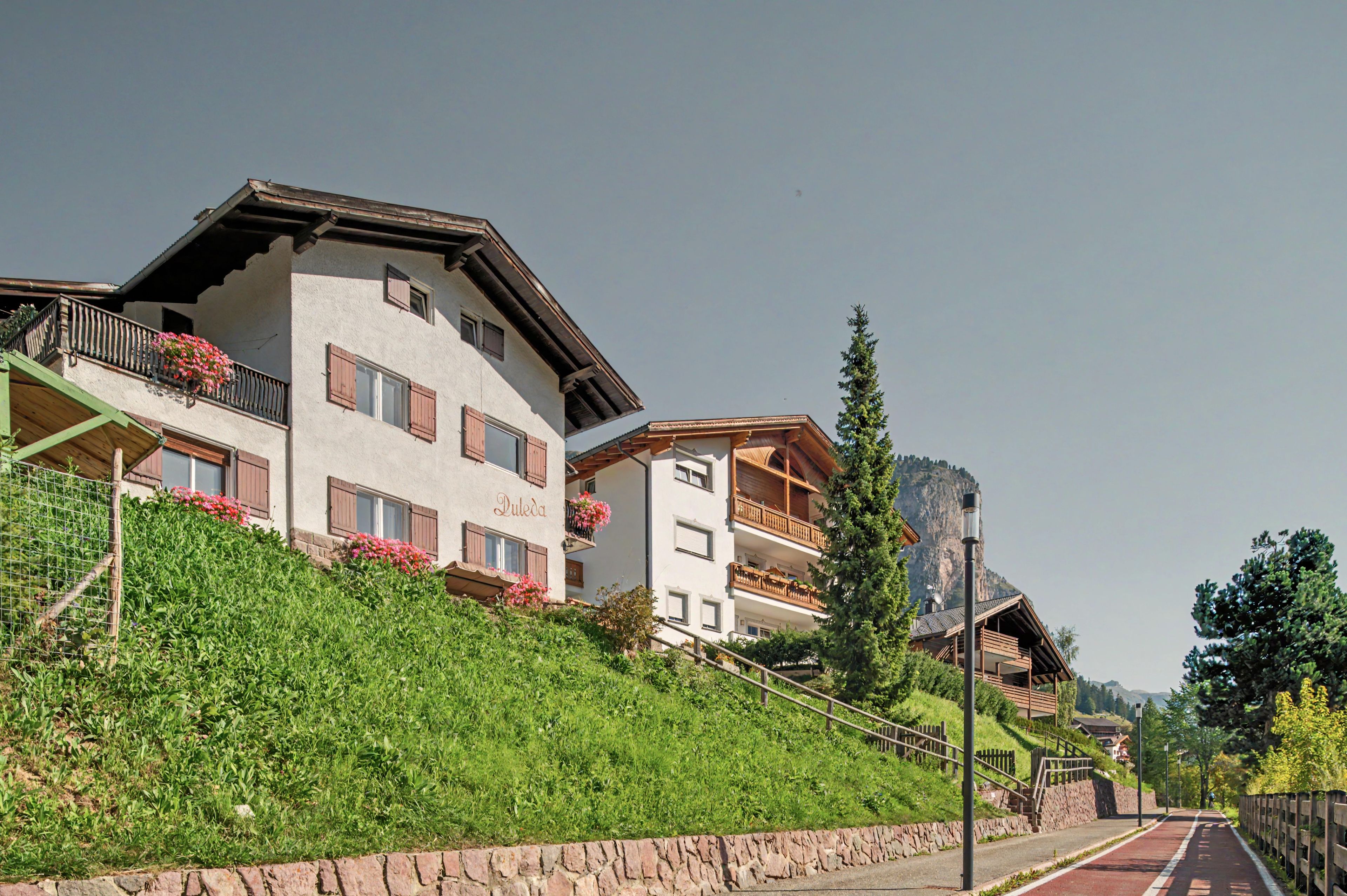 A multi-story building with balconies, a stone retaining wall, and a clear sky.