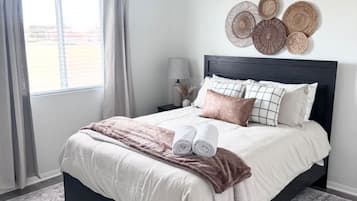 Un dormitorio con cama, ventilador de techo, ventana con cortinas, mesita de noche con lámpara y decoración mural.