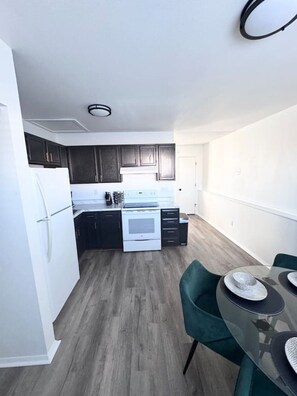 A modern kitchen with dark cabinets, a white refrigerator, and a built-in oven.